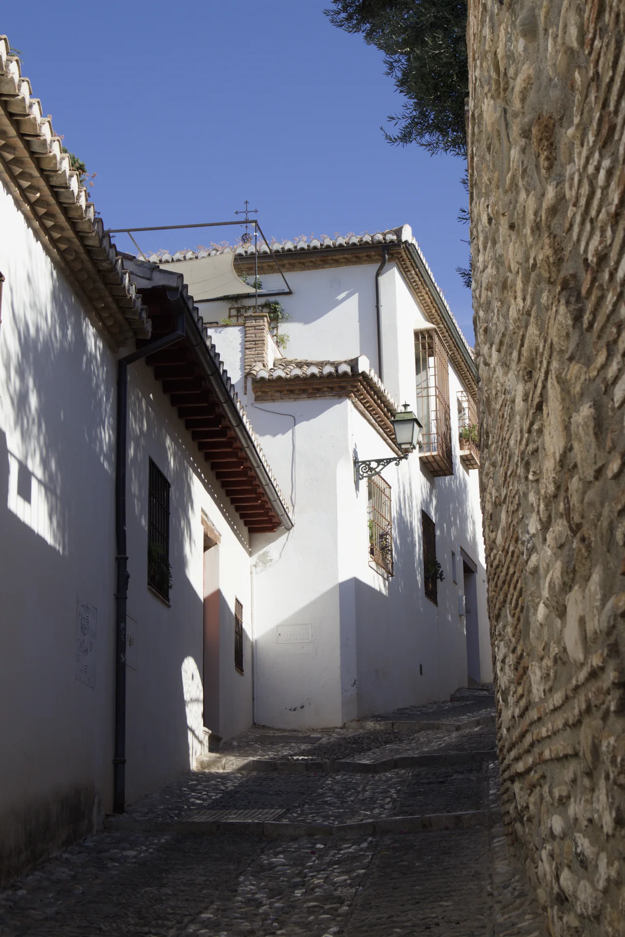Calle estrecha encalada del Albaicín con la colina de la Alhambra al fondo